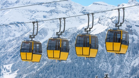 Vier gelbe Seilbahngondeln, im Hintergrund winterliche Berglandschaft