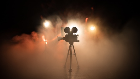 Alte Filmkamera mit Analogfilmspulen im Gegenlicht umgeben von Nebel in rotgelbem Licht