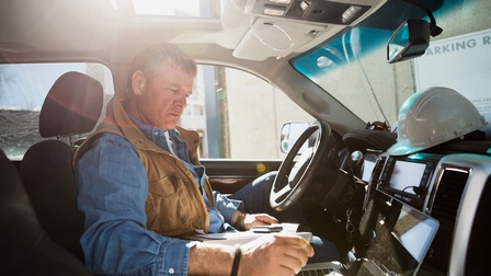 Person sitz auf Fahrersitz in Auto und bedient aufgeklappten Laptop
