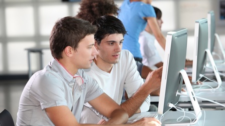 Zwei Personen sitzen vor Computerbildschirm