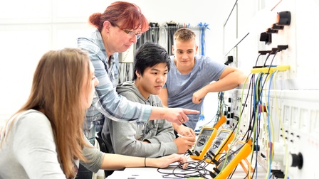 Lehrperson weist drei Lehrlinge in elektrotechnische Gerätschaften ein