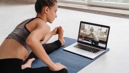 Eine Frau in Sportbekleidung macht Dehnübungen mit einer Fitnesstrainerin über Webkamera