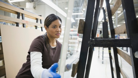 Eine Person mit Handschuhen schiebt eingepackte Glasscheiben durch eine Werkstatt