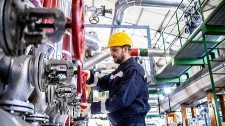 Person in Schutzbekleidung mit Schutzhelm arbeitet in einer Raffinerie