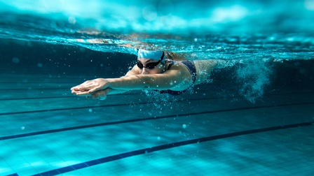 Unter Wasseraufnahme einer Person mit Badekappe, Schwimmbrille und Badeanzug, die mit ausgestreckten Armen im Wasser eines Sportbeckens taucht