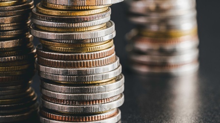 Nahaufnahme dreier Münzstapel auf einer dunklen Oberfläche.