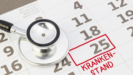 Nahaufnahme eines Kalenderblattes, in dem um die Zahl fünfundzwanzig ein roter Rahmen gelegt ist. Darunter steht Krankenstand in roter Schrift. Auf dem Kalender liegt ein Stethoskop