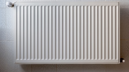 Ein weißer Heizkörper ist erhöht an einer verfliesten Wand montiert