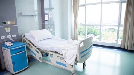 Helles, menschenleeres Krankenhauszimmer mit Krankenbett 