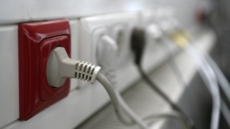 Nahaufnahme einer roten Steckdose, im Hintergrund sind weitere Steckdosen mit angeschlossenen Steckern