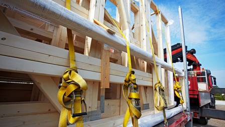 Fokus auf eine Holzkonstruktion, die auf einem Schwertransporter beladen ist und mit Ladegurten gesichert wird