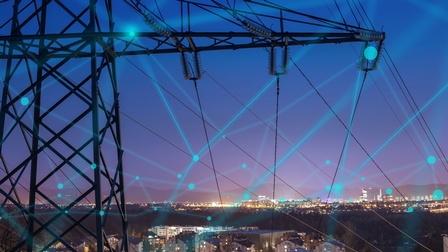 Im Vordergrund im Ausschnitt Strommasten mit blauem Overlay zu Punkten zusammenlaufender Linien ein Netz formend, im Hintergrund Stadtlandschaft im Abendlicht