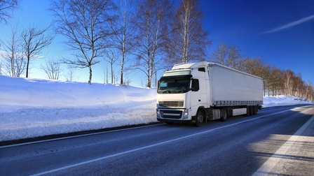 Weißer LKW fährt entlang einer Straße mit Winterlandschaft und Schnee