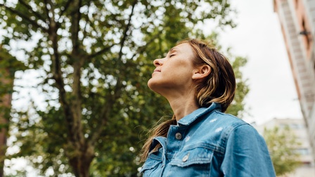 Porträt einer Person, die im Freien steht, die Augen geschlossen hat und atmet.