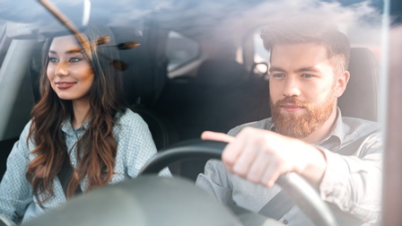Zwei sanft lächelnde Personen in Auto sitzend, eine Person lenkend
