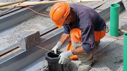 Porträt von Person in Schutzkleidung und orangen Schutzhelm beim Straßenbahnschienenbau