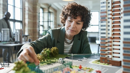 Person in Businesskleidung arbeitet an einem Ausschnitt eines Modells mit Wohnbau- und Grünanlagen