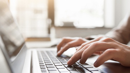 Nahaufnahme von zwei Händen, die auf der Tastatur eines aufgeklappten Laptops tippen