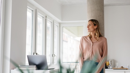 Junge Frau steht im Homeoffice an einer Säule und denkt über die Zukunft nach
