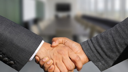 Nahaufnahme zweier Personen in Anzügen, die sich die Hände schütteln