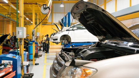 Mehrere Autos mit geöffneten Motorhauben, zwei Personen werkend