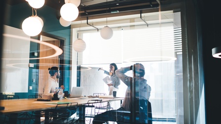 Drei Personen arbeiten mit Whiteboard und Dokumenten in modernem Konferenzraum
