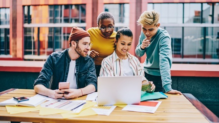 Gruppe junger Personen vor Laptop versammelt, im Hintergrund Hausfassade