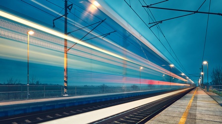 Bahngleis und Bahnsteig im Dämmerlicht im Fokus, ringsum bewegungsunscharfe Lichtlinien