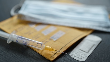 Nahaufnahme eines Impfpasses, einer Spritze, eines Pflasters und eines Mundschutzes