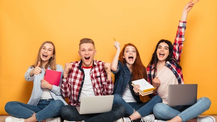 Vier junge Personen sitzen vor einer gelben Wand und freuen sich