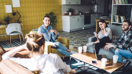 Gruppe junger Personen in buntgemustertem Raum auf Couchmöbeln sitzend unterhält sich und lacht