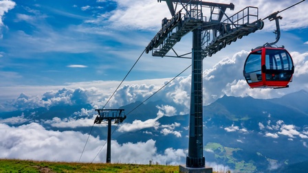 Im Vordergrund rote Seilbahngondel, im Hintergrund Berglandschaft mit Wolken