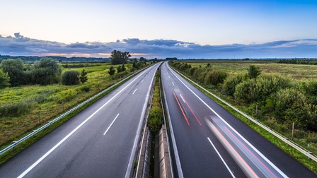 Blick auf Autobahn mit vorbeifahrenden Autos in Bewegungsunschärfe bei Sonnenuntergang 