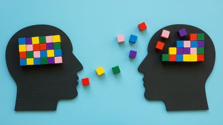 Illustration zweier Köpfe, im Bereich des Gehirns sind bunte Würfel platziert, vor dem Mund eines Kopfes sind weitere bunte Würfel in Richtung des anderen Kopfes verstreut.