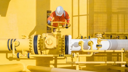Person in Arbeitskleidung mit Schutzhelm arbeitet in einer Raffinerie mit gelber Oberfläche