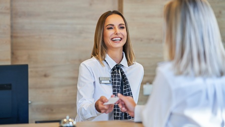 Rezeptionistin übergibt an der Rezeption lachend eine Schlüsselkarte an Kundin