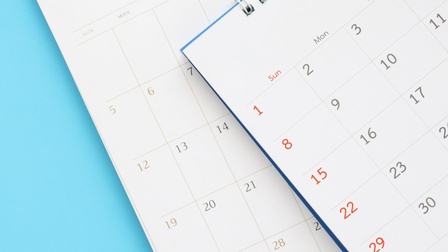 Nahaufnahme zweier übereinander, leicht versetz, liegender Ausschnitte von Kalenderblättern vor blauem Hintergrund