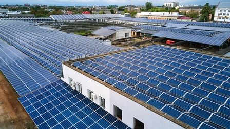 Hallen und Gerüste voller Solarpanele, im Hintergrund Stadtansicht unter bewölktem Himmel