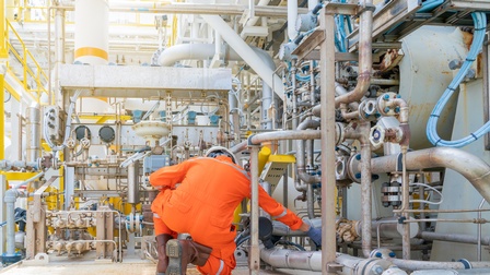 Person in orangem Schutzanzug in Rückenansicht kontrolliert auf Boden kniend Leitungen