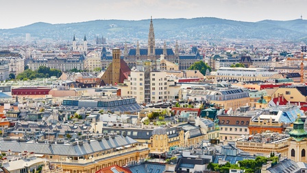 Panoramaaufnahme Teile der Stadt Wiens mit verschiedenen Sehenswürdigkeiten im Vordergrund. Im Hintergrund sind weitere Gebäude und Hügel