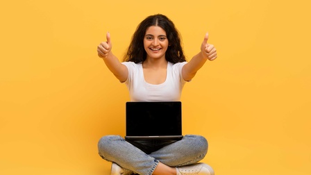 Eine junge Frau sitzt im Schneidersitz auf dem Boden mit einem Laptop auf dem Schoß