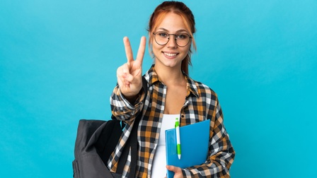 Person mit Brillen in kariertem Hemd mit Rucksack um die Schulter gehängt hält in einer Hand blaue Mappe mit Stift und streckt die andere Hand von sich weg mit ausgestrecktem Zeige - und Mittelfinger, Hintergrund blau