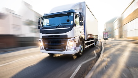 Im Fokus weißer Lastkraftwagen in frontaler Ansicht, Umgebung bewegungsunscharf