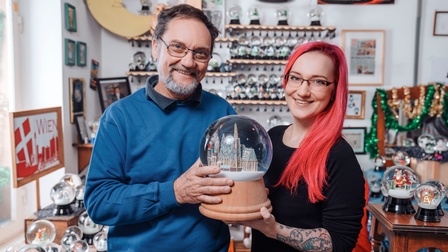 Zwei lächelnde Personen mit Brillen halten große Schneekugel in Händen