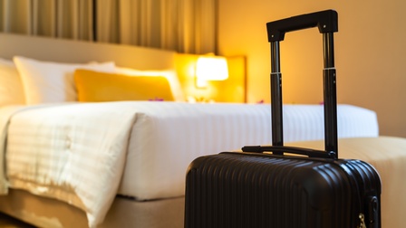 Ein schwarzer Koffer steht vor einem Bett in einem Raum mit indirekter Beleuchtung