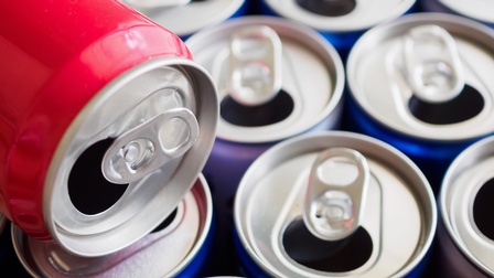 Detailansicht mehrerer geöffneter blauer Getränkedosen, eine rote Dose auf stehenden Dosen liegend