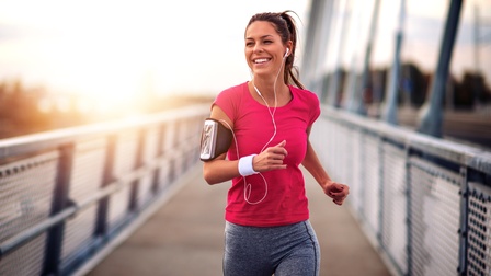 Lächelnde Person in Sportkleidung und Kopfhörer joggt über eine Brücke