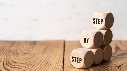 Holzwürfel aufeinandergestapelt mit Schriftzug step by step