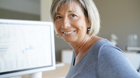 Porträt einer lächelnden Person an Schreibtisch vor Computer sitzend