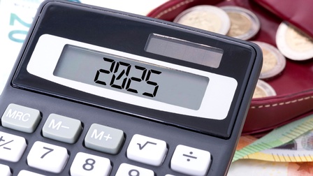 Nahaufnahme eines Taschenrechners, auf dem 2025 steht. Dahinter sind verschiedene Euroscheine sowie Euromünzen.